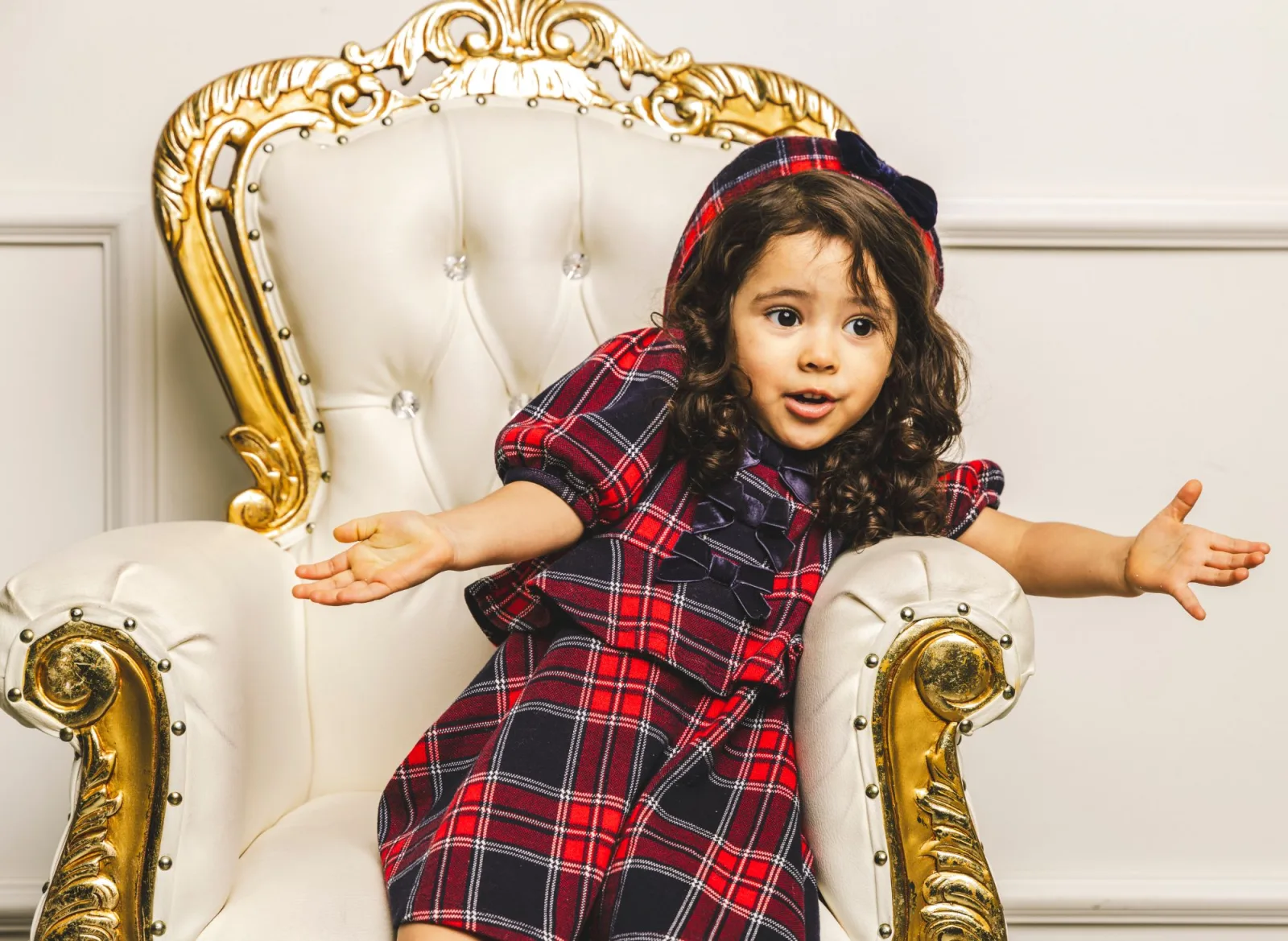 Toddler shrugging with both hands out, seated in a gold and cream armchair