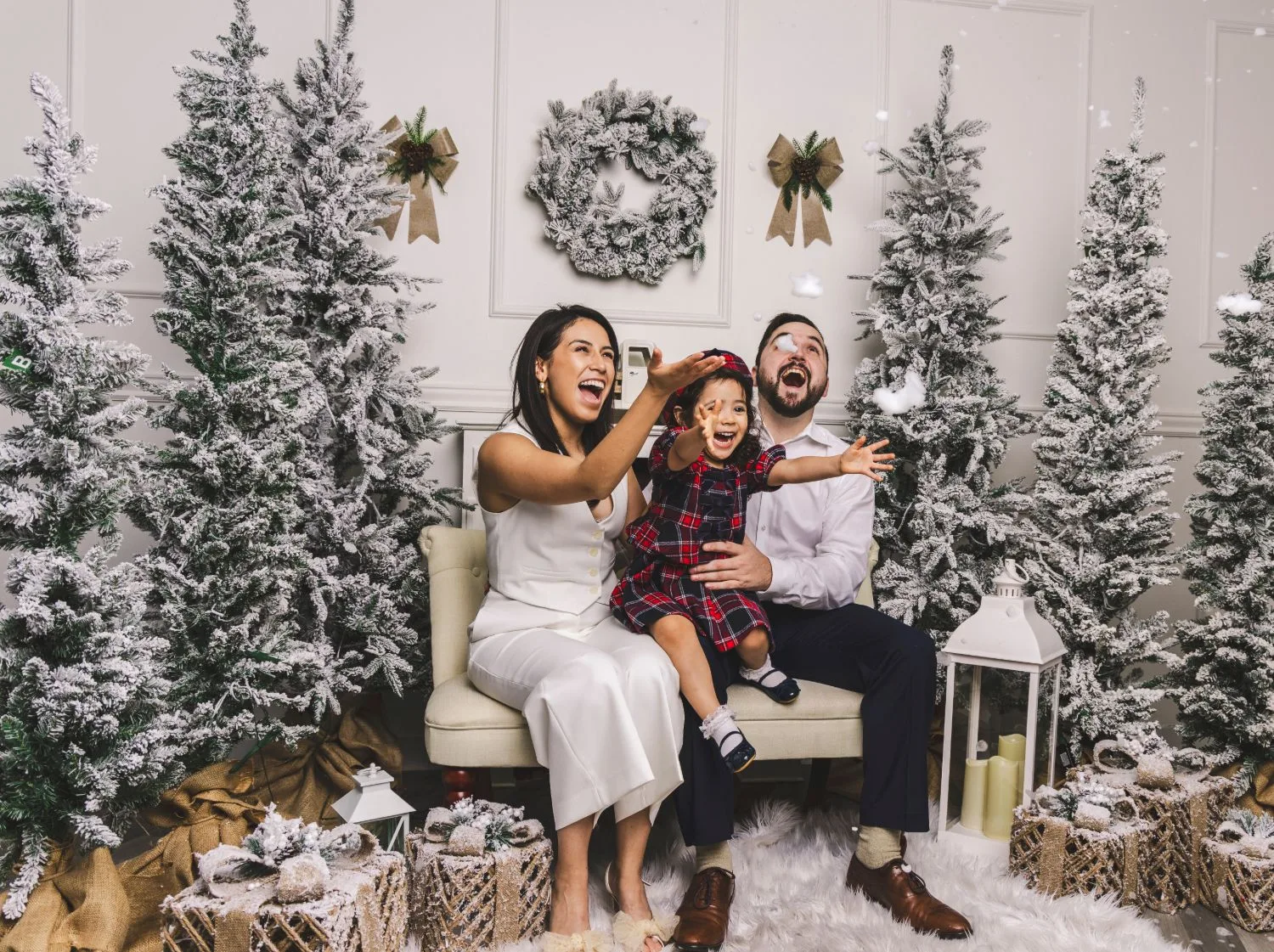 Family of three laughing as fake snow falls in a flocked-tree studio set