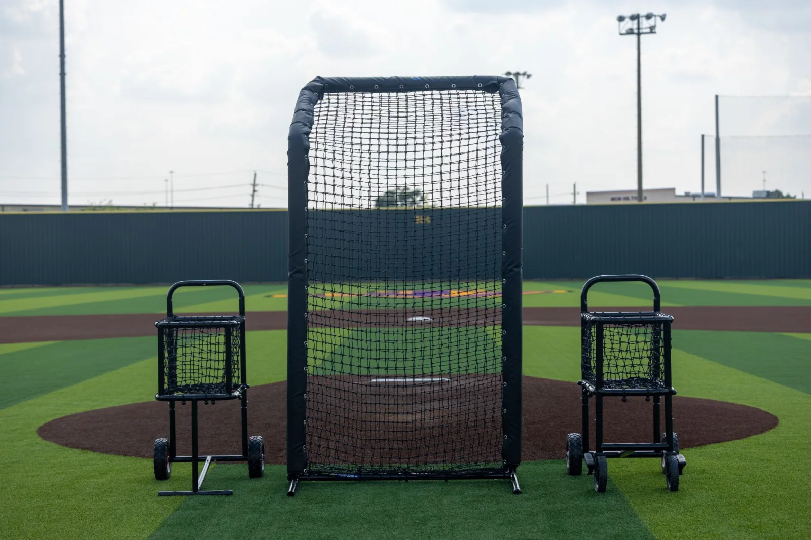 Padded pitching screen staged at the mound between two ball carts