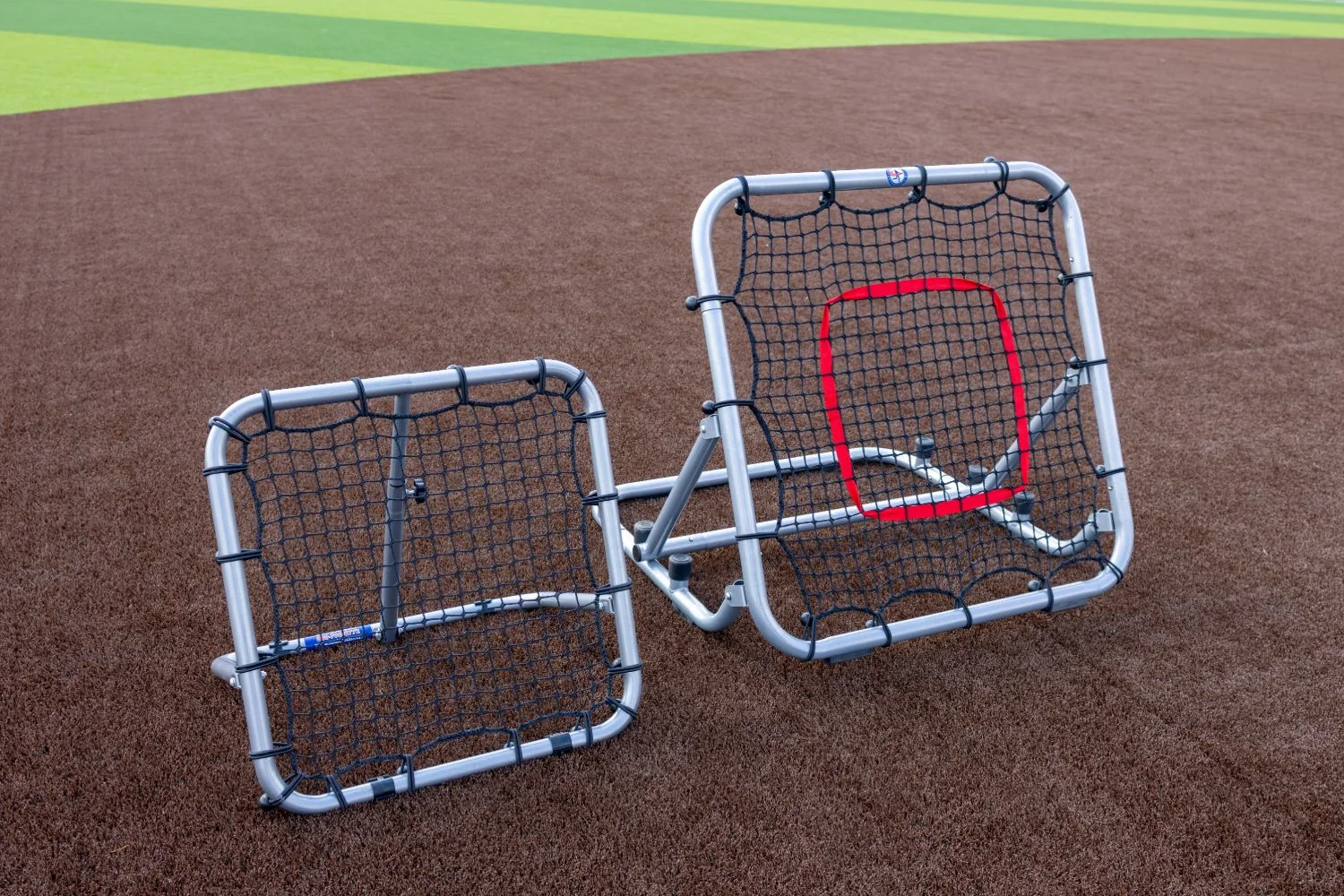 A pair of rebounder trainers staged together on striped infield turf
