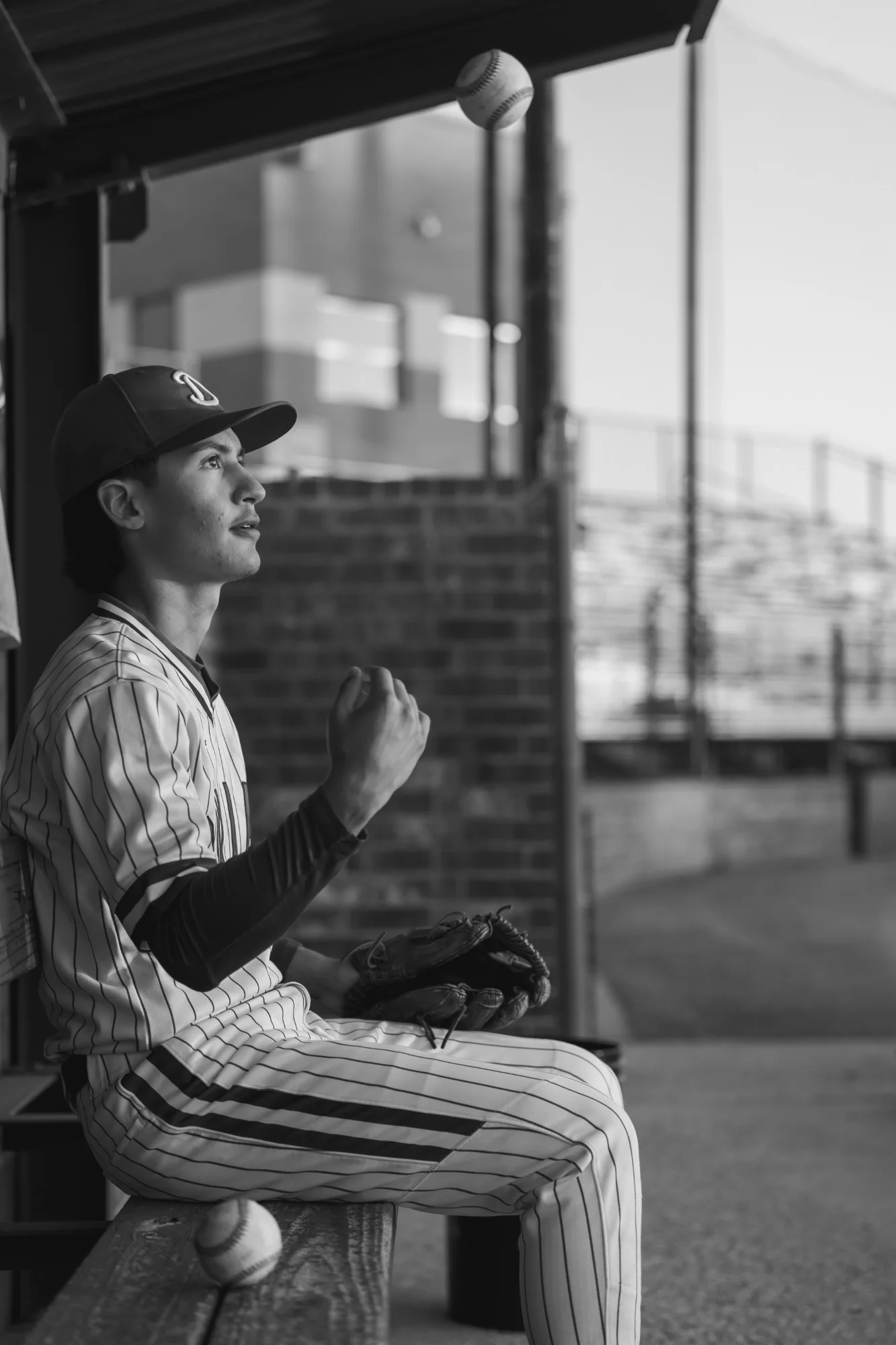 Black and white frame of a senior seated in the dugout with his glove
