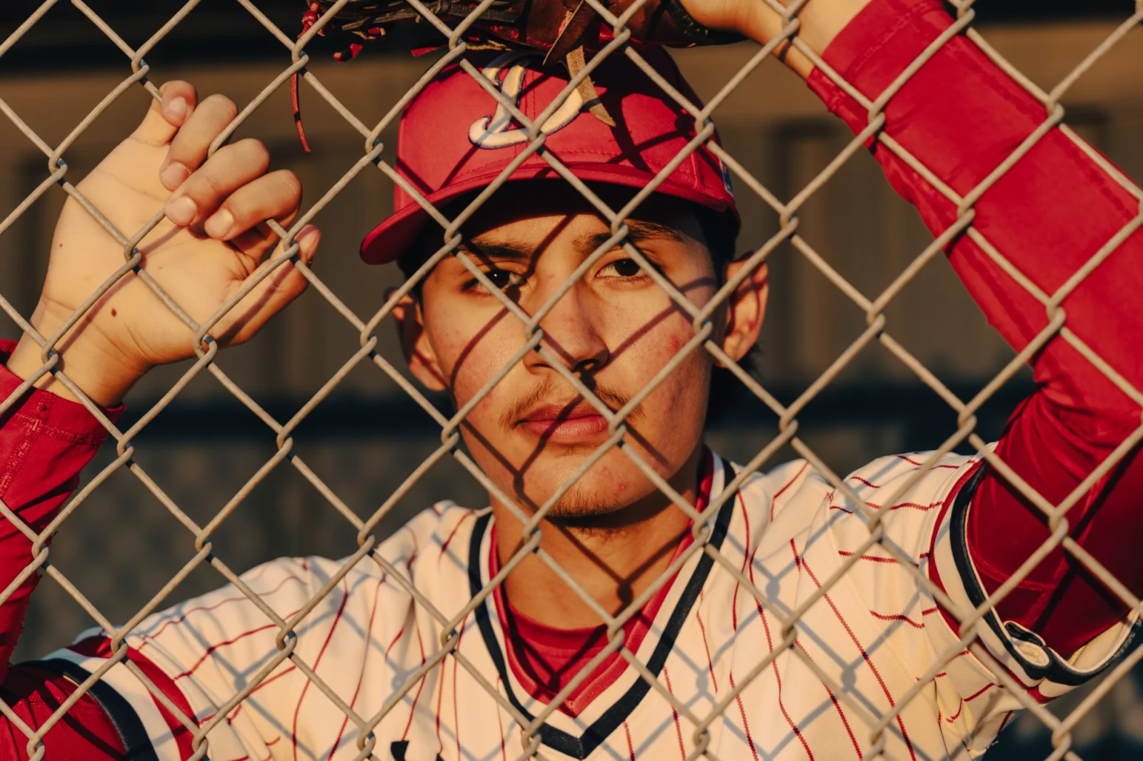 Close portrait of a senior through the backstop fence in cap and uniform