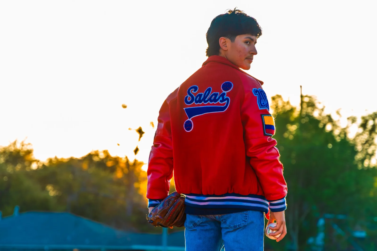 Senior walking away at sunset with his name across the back of his letter jacket