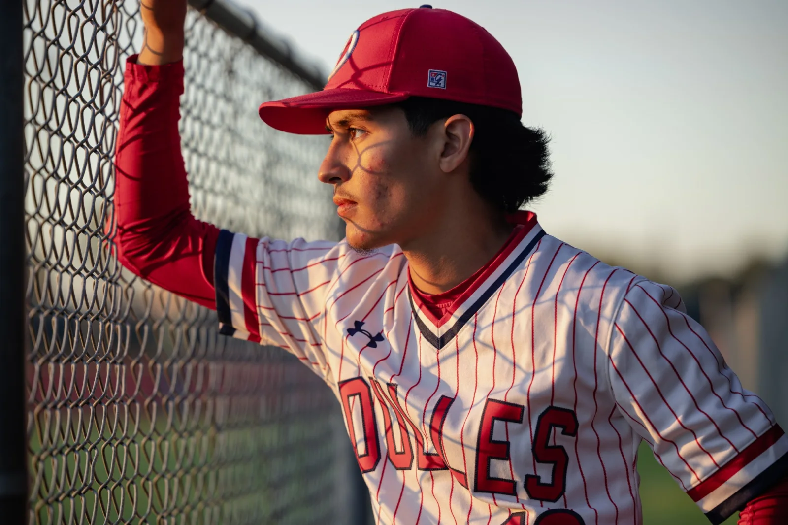 Senior in his baseball uniform leaning against the outfield fence